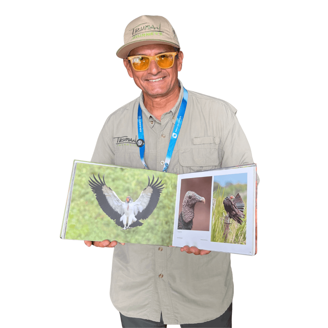 Hombre de gorra y gafas amarillas que muestra un libro abierto con fotos de aves.